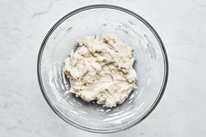 gluten free pizza dough being stirred in a bowl made with gluten free flour, salt, instant dry yeast, warm water & olive oil