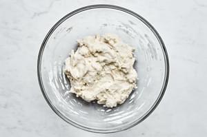 gluten free pizza dough being stirred in a bowl made with gluten free flour, salt, instant dry yeast, warm water & olive oil
