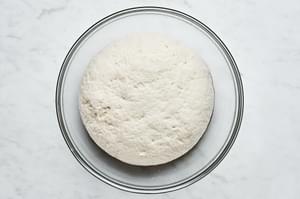 gluten free pizza dough ball in a glass bowl after it has risen and doubled in size