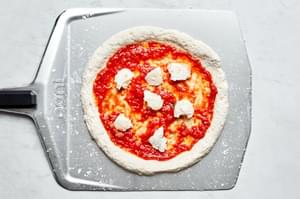 homemade gluten free pizza dough topped with marinara and cheese on a pizza peel