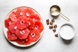 a plate of grape fruit slices, a cup of sugar, a cup of water and 6 star anise