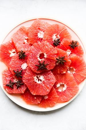 slices of red grapefruit on a plate with star anise simple syrup