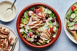 Greek Grilled chicken with salad topped with cucumbers, tomatoes cucumbers, sliced  Kalamata olives and red onion