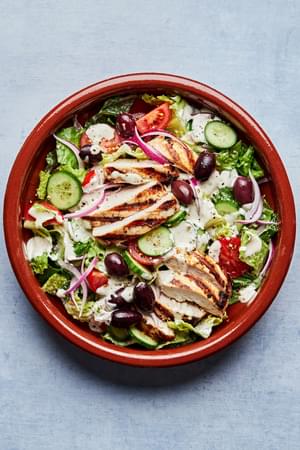 Greek Grilled chicken with salad topped with cucumbers, tomatoes cucumbers, sliced  Kalamata olives and red onion