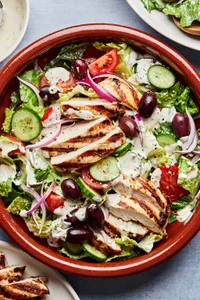 Greek Grilled chicken with salad topped with cucumbers, tomatoes cucumbers, sliced Kalamata olives and red onion