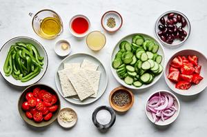 cucumbers, bell peppers, tomatoes, red onion, kalamata olives, olive oil, lemon juice, red wine vinegar and spices in bowls