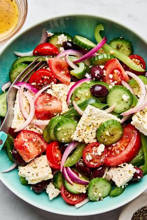 greek salad in a serving bowl made with cucumbers, bell peppers, tomatoes, red onion, kalamata olives and greek dressing