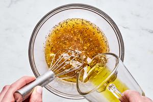 vinegar, lemon juice, garlic, mustard, salt, oregano and pepper being whisked together in a bowl