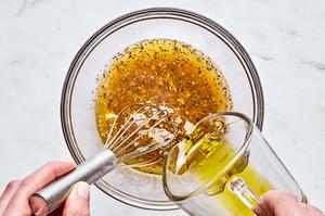 vinegar, lemon juice, garlic, mustard, salt, oregano and pepper being whisked together in a bowl