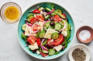 a large bowl of greek salad surrounded by salt, pepper and greek salad dressing
