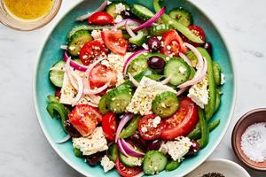 greek salad in a serving bowl made with cucumbers, bell peppers, tomatoes, red onion, kalamata olives and greek dressing