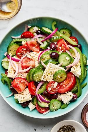greek salad in a serving bowl made with cucumbers, bell peppers, tomatoes, red onion, kalamata olives and greek dressing