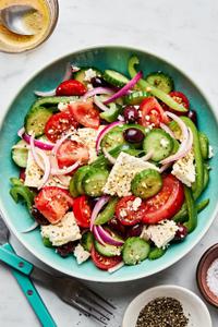 greek salad in a serving bowl made with cucumbers, bell peppers, tomatoes, red onion, kalamata olives and greek dressing