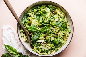 pasta salad with green goddess dressing and olives, asparagus, spinach, green onions in a bowl with a serving spoon
