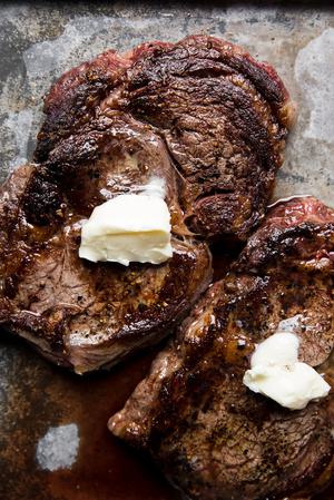2 grilled rib eye steaks resting on a baking sheet with butter