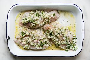 3 tilapia filets marinating in a baking dish in onions, lime juice, orange juice, oregano, garlic and cilantro
