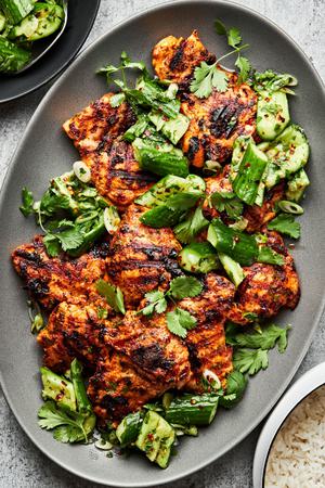 Grilled curry chicken with smashed cucumber salad on a large serving platter with a serving fork