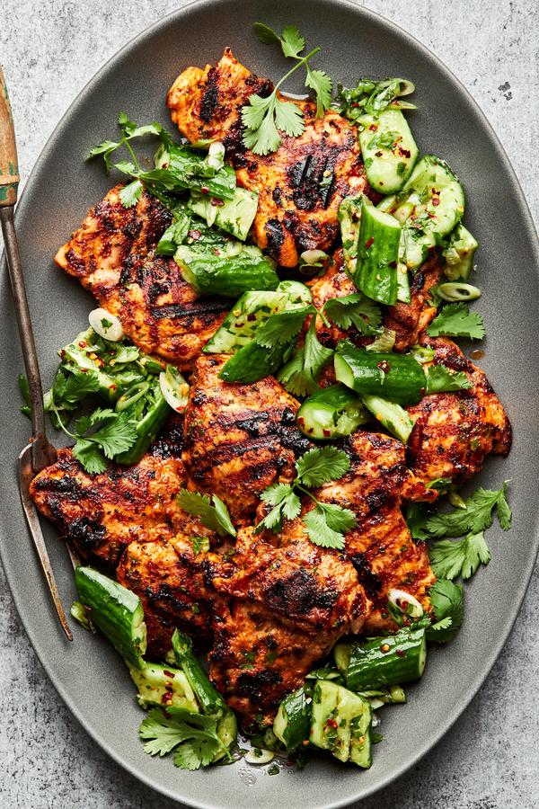 Grilled curry chicken thighs with smashed cucumber salad on a large serving platter with a serving fork