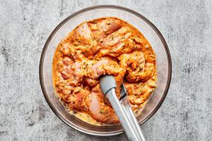 boneless, skinless chicken thighs being tossed with a red curry marinade with tongs in a glass bowl