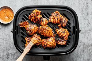 red curry marinated chicken thighs being cooked on a grill and brushed with reserved marinade