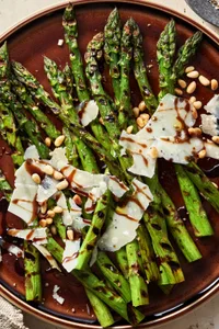 Grilled Asparagus with balsamic reduction sprinkled with parmesan cheese and pine nuts on a serving platter