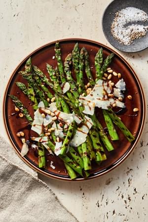 Grilled Asparagus with balsamic reduction sprinkled with parmesan cheese and pine nuts on a serving platter