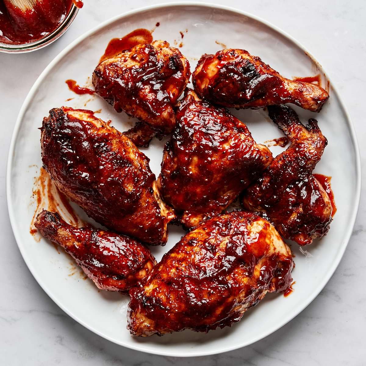 Grilled BBQ chicken pieces on a serving plate being brushed with a thick, glossy homemade barbecue sauce