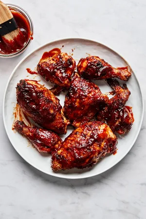 Grilled BBQ chicken pieces on a serving plate being brushed with a thick, glossy homemade barbecue sauce