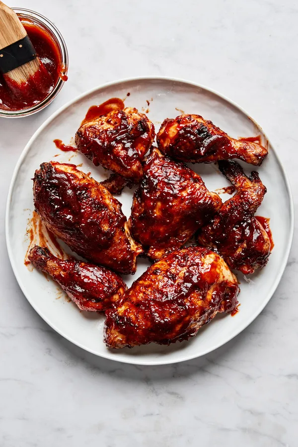 Grilled BBQ chicken pieces on a serving plate being brushed with a thick, glossy homemade barbecue sauce