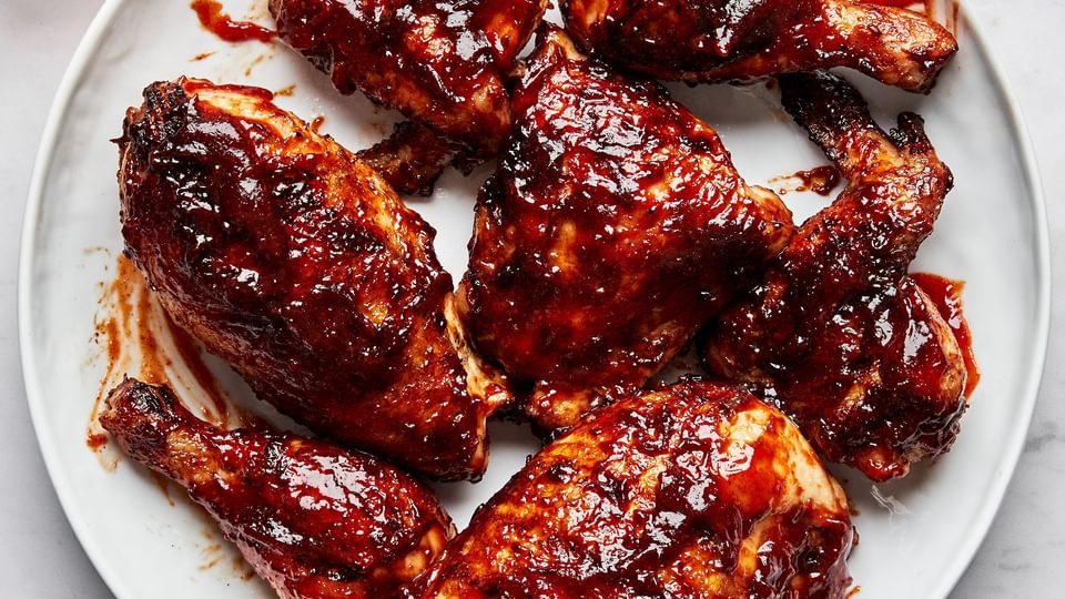 Grilled BBQ chicken pieces on a serving plate being brushed with a thick, glossy homemade barbecue sauce