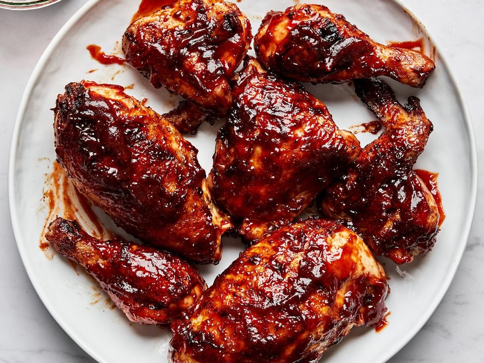 Grilled BBQ chicken pieces on a serving plate being brushed with a thick, glossy homemade barbecue sauce