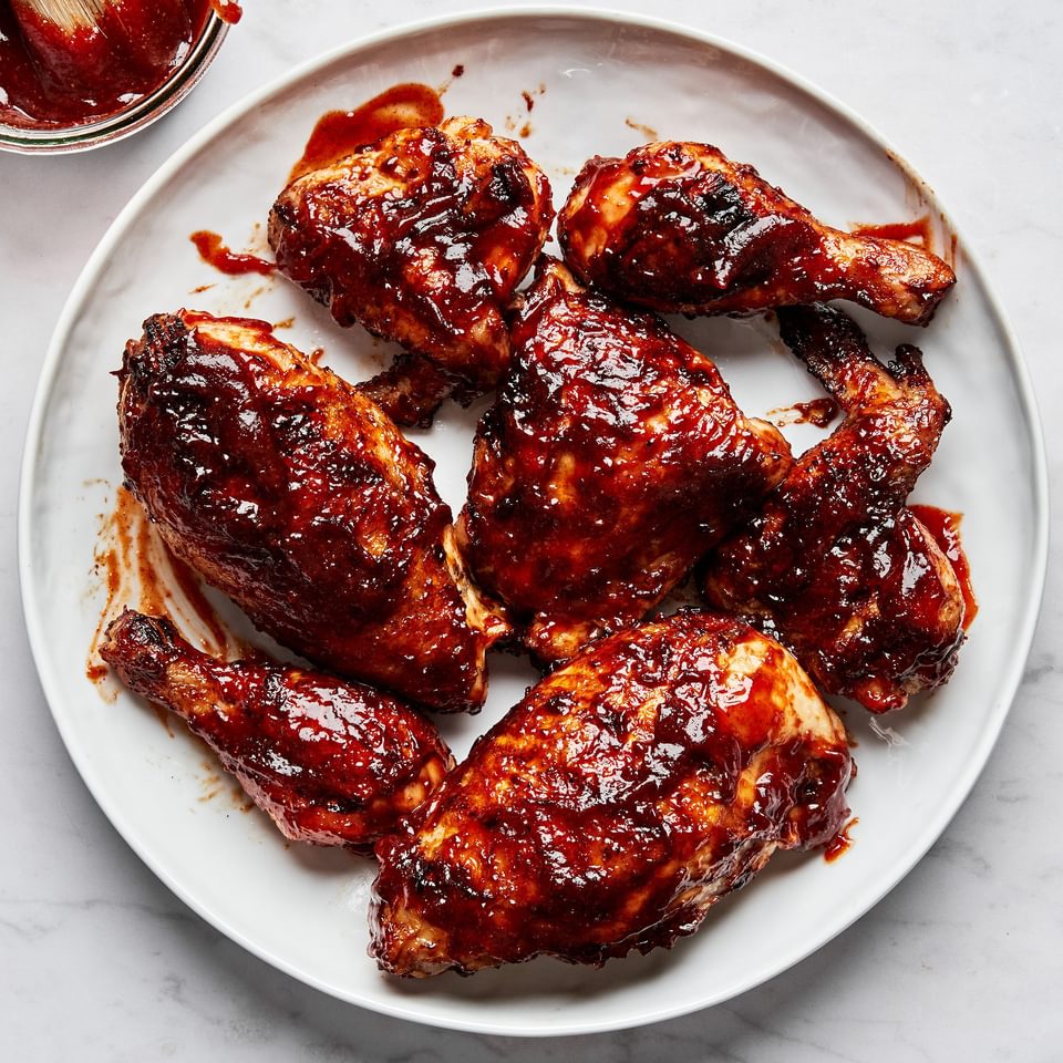 Grilled BBQ chicken pieces on a serving plate being brushed with a thick, glossy homemade barbecue sauce
