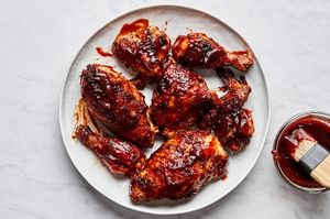 Grilled BBQ chicken pieces on a serving plate being brushed with a thick, glossy homemade barbecue sauce