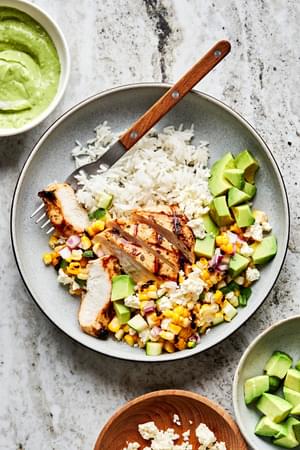 Grilled Chicken Bowl with corn and zucchini salad served on top of white rice in a bowl with a fork