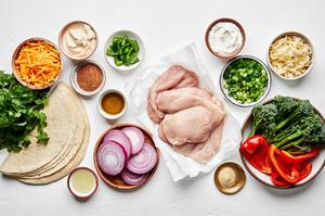 raw chicken breast, bell pepper, red onion, broccolini, tortillas, cheese, cilantro, and spices in prep bowls