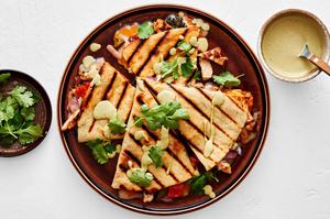 a grilled chicken quesadilla sliced in wedges on a plate drizzled with jalapeño ranch and sprinkled with cilantro
