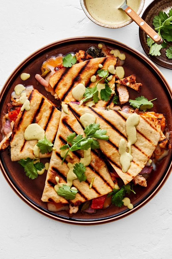 a grilled chicken quesadilla cut in wedges on a plate drizzled with jalapeño ranch and sprinkled with cilantro