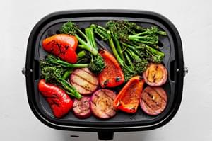 bell peppers, broccolini, and red onion tossed with olive oil and taco seasoning being cooked on the grill