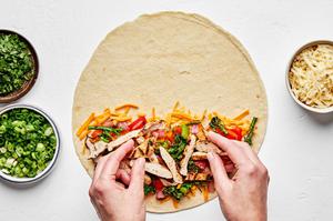 a flour tortilla being filled with cheese, grilled onion, peppers, broccolini and chicken