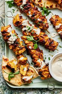 grilled chicken shawarma kebabs on a serving platter drizzled with tahini sauce served with pita bread