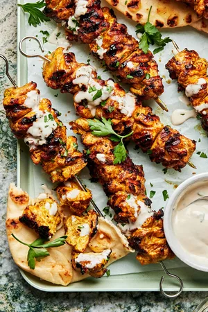 grilled chicken shawarma kebabs on a serving platter drizzled with tahini sauce served with pita bread