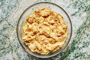 raw chicken marinating in yogurt, cumin, cardamom, turmeric, cinnamon, and salt in a glass bowl
