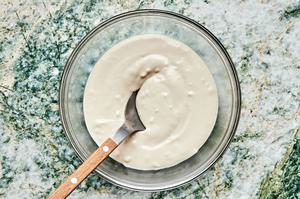 tahini sauce being stirred with a spoon in a glass bowl made with tahini, lemon juice, garlic, water, and salt