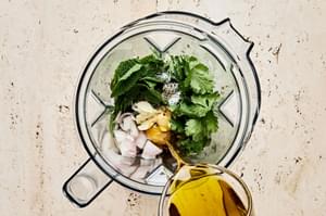 shallot, olive oil, vinegar, mustard, honey, garlic, salt, pepper, cilantro, and mint being combined in a blender