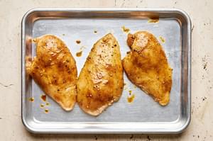 chicken rubbed with olive oil, curry powder, salt, and pepper on a baking sheet