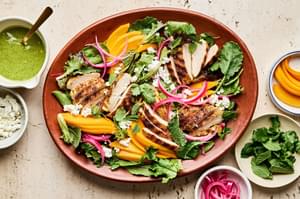 salad surrounded by toppings: mango slices, pickled onion, goat cheese, cilantro, mint, and herb vinaigrette