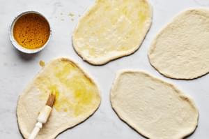 pizza dough rolled out into 4 small flat breads, being brushed with olive oil