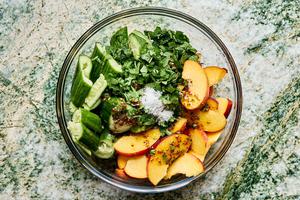 cucumbers, peaches, cilantro, mint, lemon juice, honey mustard dressing & salt being tossed in a bowl