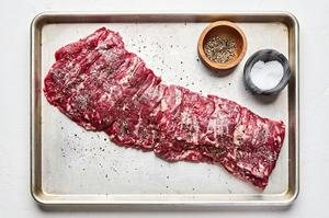a skirt steak being seasoned with salt and pepper
