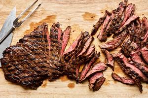 grilled skirt steak being sliced thinly on a cutting board